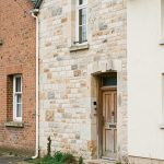Façade d’une maison ancienne présentant trois zones distinctes en brique rouge, en pierre calcaire et en crépi clair, observées sous une lumière naturelle.