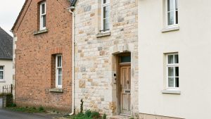 Façade d’une maison ancienne présentant trois zones distinctes en brique rouge, en pierre calcaire et en crépi clair, observées sous une lumière naturelle.