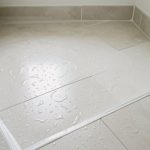 Sol de salle de bains carrelé autour d’une douche récemment installée, avec des joints en silicone soignés et des gouttes d’eau formant des perles à la surface.
