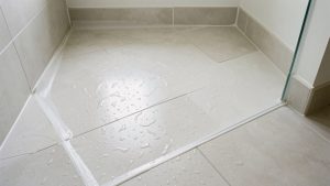 Sol de salle de bains carrelé autour d’une douche récemment installée, avec des joints en silicone soignés et des gouttes d’eau formant des perles à la surface.
