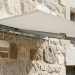 Store banne fixé de manière sécurisée sur un mur en pierre friable avec une platine métallique renforcée et des ancrages répartissant la charge.
