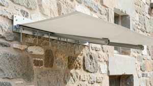 Store banne fixé de manière sécurisée sur un mur en pierre friable avec une platine métallique renforcée et des ancrages répartissant la charge.