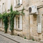 Maison ancienne en pierre dans une rue patrimoniale française, avec une unité extérieure de climatisation discrètement installée sur la façade arrière.