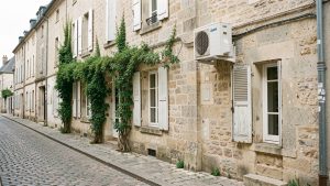 Maison ancienne en pierre dans une rue patrimoniale française, avec une unité extérieure de climatisation discrètement installée sur la façade arrière.